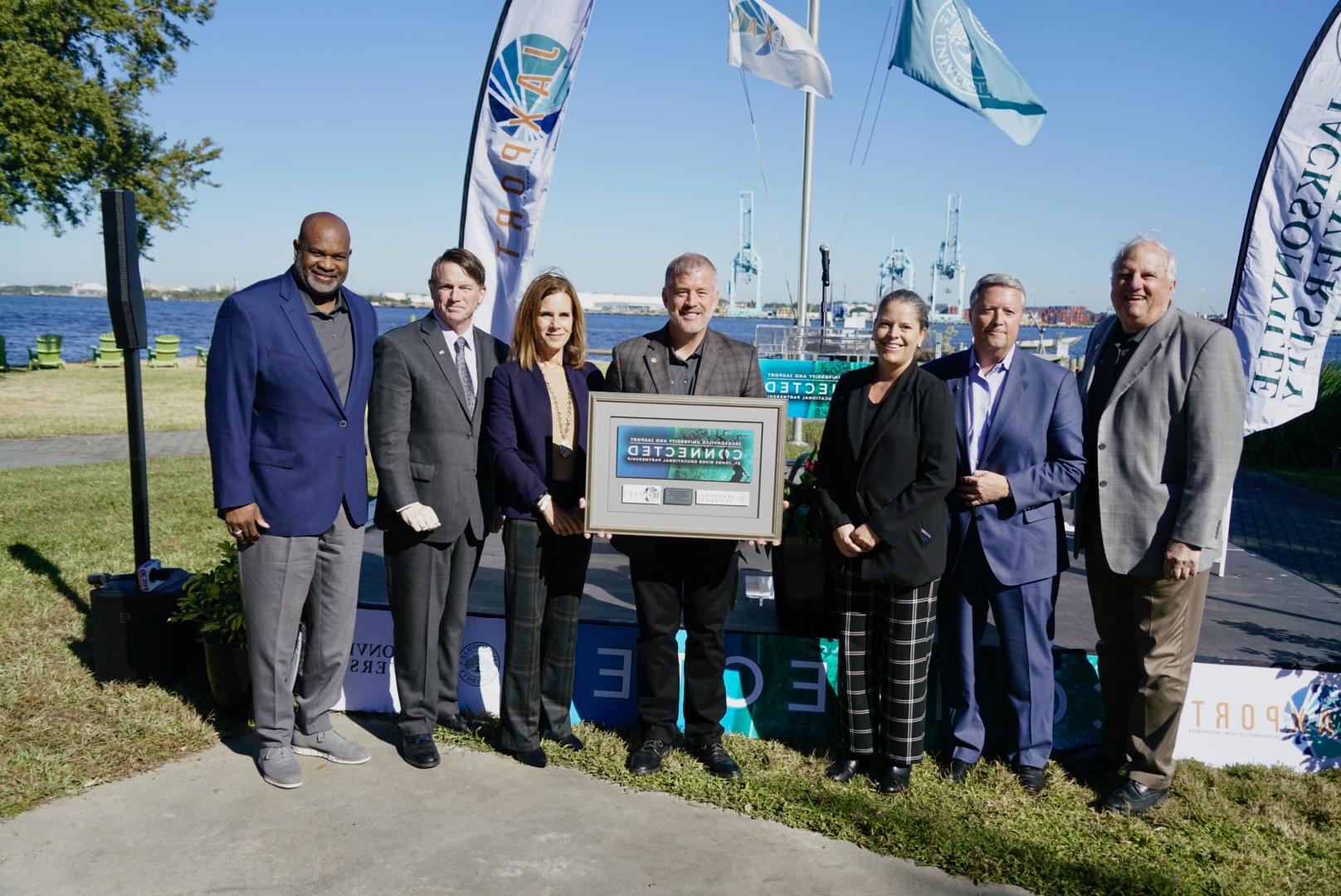 A group of Executives holding a Connected plack at Jacksonville University St John's River docs.